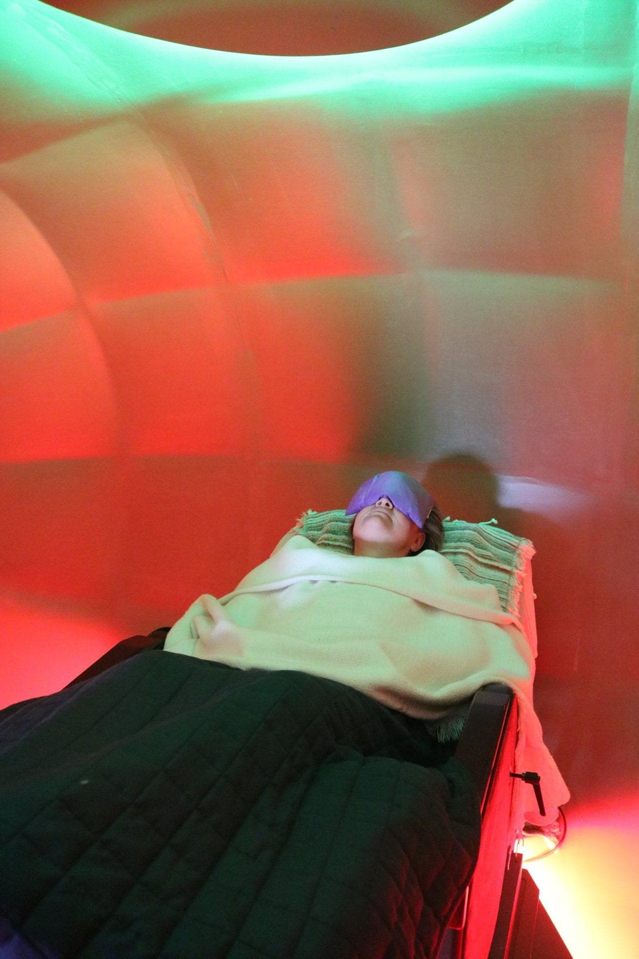 A client resting under a blanket with an eye mask in violet light