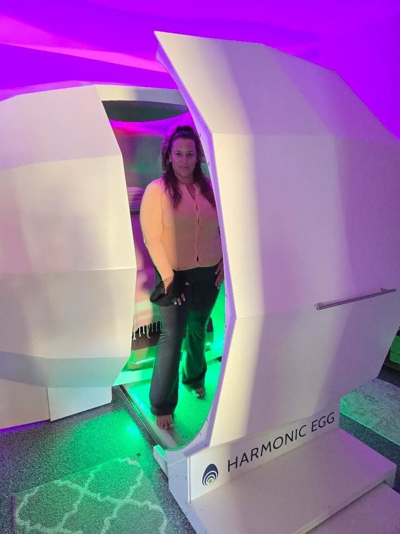 A client at the open Harmonic Egg, lit green and magenta